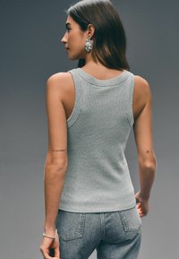 Grå ribbet strik tanktop med rund halsudskæring, pralende med brede skulderstropper. Sammen med grå denimjeans, der viser en slank pasform.