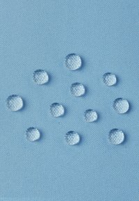 Water droplets beading on light blue textured fabric, demonstrating water-resistant or hydrophobic material properties.