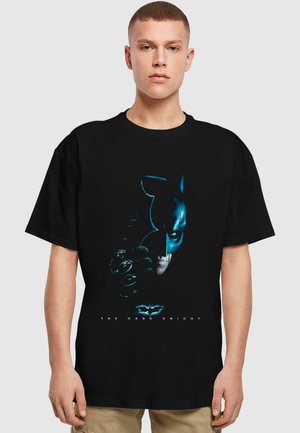 Camiseta negra con un estampado gráfico de la cara de Batman y su guantelete en tonos azules y grises, con el texto "EL CABALLERO OSCURO" debajo.