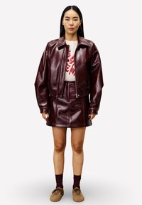 Bordeaux leren jack met een oversized pasvorm, gecombineerd met een bijpassende leren minirok. Model draagt een graphic sweatshirt eronder.
