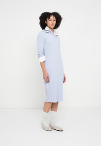 Lys blå, ribbestrikket kjole med hvit skjorte med krage under. Kjolen har lange ermer og en midt-lang lengde. Brukes med grå flate sko og hvite sokker.