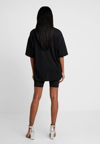 Czarny, oversize t-shirt wykonany z bawełny, w połączeniu z czarnymi szortami i srebrnymi sandałami na obcasie. Proste czarne włosy sięgają poza ramiona.