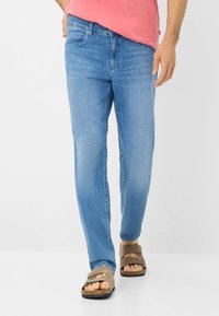 Jeans in denim blu chiaro con vestibilità dritta, dotati di tasche posteriori e una leggera scoloritura. Abbinati a sandali marroni a infradito.
