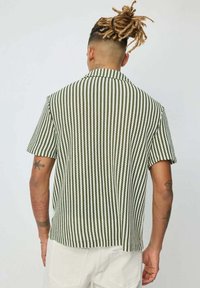 Chemise à manches courtes rayée verte et blanche avec col, coupe décontractée et tissu texturé. Présente un ourlet droit et des évents sur les côtés.