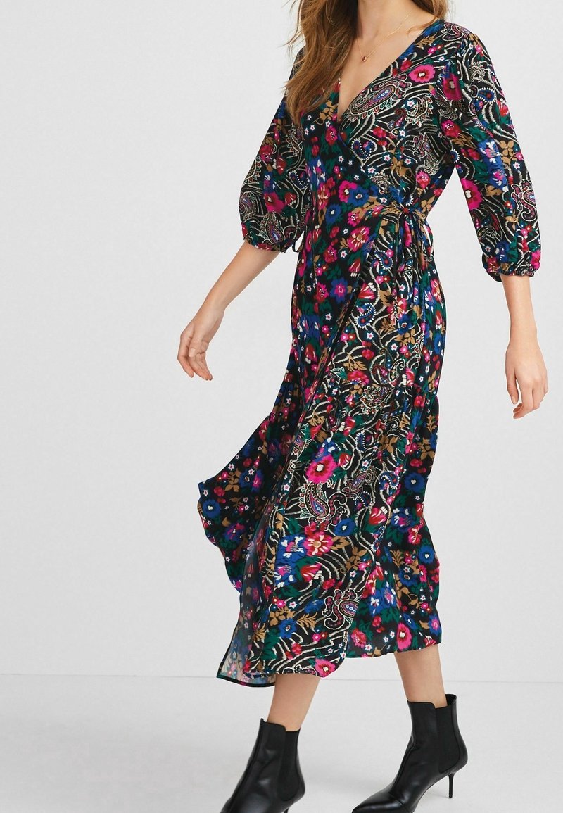Robe à motif floral en bleu foncé, avec un design portefeuille, des manches ballon et une jupe fluide. Portée avec des bottines noires.