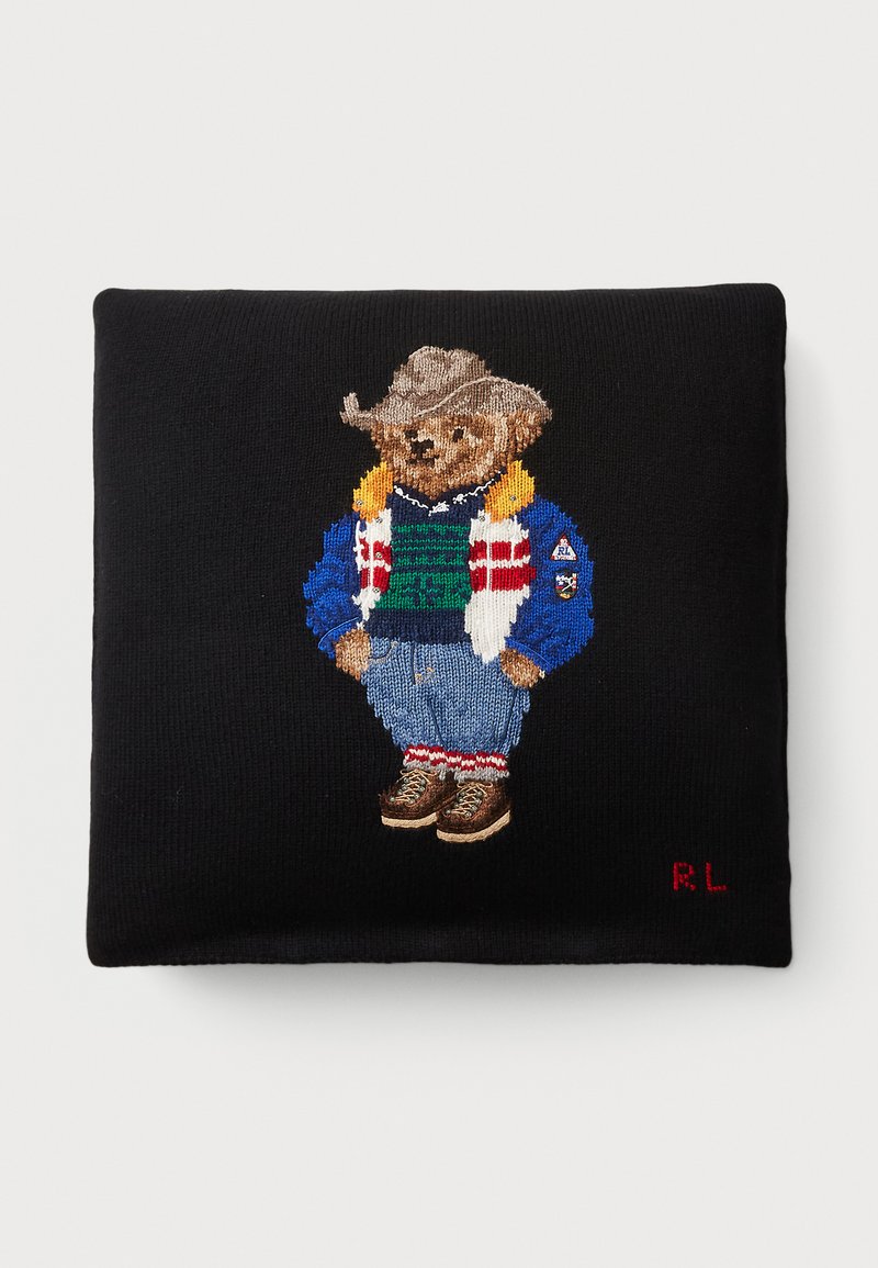 Schwarzes Strickkissen mit einem gestickten Bären, der einen beigen Cowboyhut, eine bunte Jacke, einen grünen Pullover, eine blaue Jeans und braune Stiefel trägt.