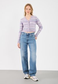 Fialový zkrácený cardigan se pruhovaným vzorem, spárovaný s modrými džíny s vysokým pasem. K outfitu se dokonale hodí tenisky s krémovými, šedými a vínovými akcenty.