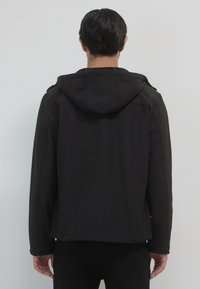 Giacca nera con cappuccio realizzata in un tessuto morbido e testurizzato. Caratterizzata da una vestibilità rilassata, spalle senza cuciture e orlo dritto, progettata per il massimo comfort.