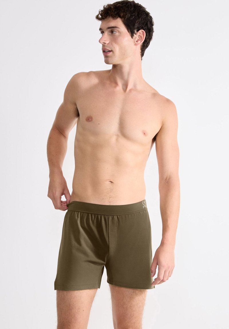 Olijfgroene heren shorts met een elastische tailleband, gemaakt van gladde stof. Heeft een logoaccent aan de zijkant en een aansluitend ontwerp.