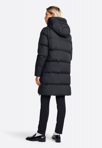 Zwarte pufferjack met een capuchon, voorzien van een gewatteerd ontwerp, lange mouwen en een middellange snit. Draag het over zwarte jeans en schoenen.