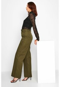 Zwarte sheer lange mouw top met zebra strepen, gecombineerd met olijfgroene high-waisted cargo pants. De broek heeft zijzakken en een ceintuur in de taille.