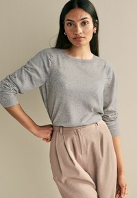 Grauer Pullover mit gesprenkeltem Muster und gerippten Bündchen, kombiniert mit hochtaillierten beigefarbenen Hosen. Einfaches, strukturiertes Design.