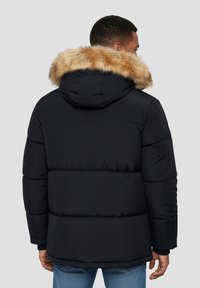 Chaqueta acolchada negra con capucha desmontable forrada de piel sintética color beige, textura acolchada y puños elásticos; diseñada para ofrecer calidez y comodidad.