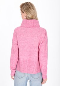 Rosa gestrickter Pullover mit hohem Rippkragen, überschnittenen Schultern und Rippdetails am Saum und den Ärmeln. Weiche Textur, lässige Passform.