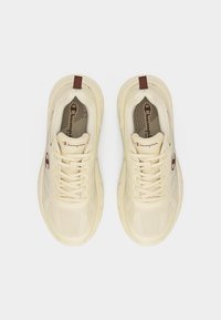 Ζευγάρι μπεζ αθλητικά παπούτσια Champion με κορδόνια, καφέ λογότυπο στα πλάγια και καφέ θηλιές, απεικονισμένα από πάνω σε λευκό φόντο.