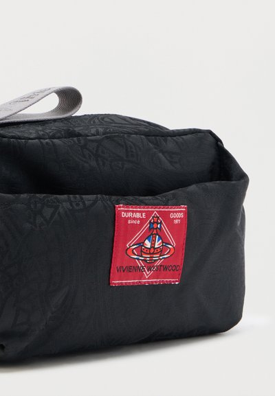 Μαύρη υφασμάτινη τσάντα με γκρι λαβή και κόκκινη ετικέτα Vivienne Westwood που απεικονίζει έναν πλανήτη και το κείμενο "Durable Goods since 1971."