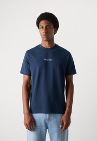 Camiseta de algodón azul marino de manga corta; presenta texto bordado en blanco "Fuera de la oficina" centrado en el pecho. Cuello redondo clásico.