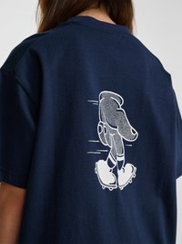 Mørkeblå skjorte med hvid grafik af en gående hånd iført podeklamper på ryggen, båret af en person med langt brunt hår.