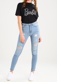 Černé tričko s kamínkovým nápisem "Barbie", kombinované se světle modrými distressed skinny džíny a bílými teniskami. Jednoduchý design a moderní střih.