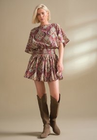 lillade, roosade ja roheliste paisley-mustriga kleit, millel on elastne vöökoht ja laienev seelik. Sobitatud pruunide põlve kõrguste seemisnahksete saapadega.