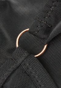 Zwarte stof met een gestructureerde afwerking, voorzien van een rosegouden metalen ring die aan een band is bevestigd, met gedetailleerde stiksels.