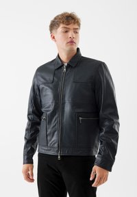Giubbotto di pelle nera con chiusura a zip, colletto alto e due tasche frontali. Presenta una texture liscia e una vestibilità su misura.