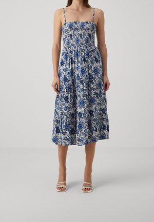 Robe florale bleue et blanche avec un corsage smocké, des bretelles spaghetti et une jupe à volants. Le tissu présente des motifs floraux complexes avec des accents jaunes.