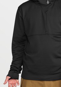 Pull noir avec un tissu texturé, doté d'une poche zippée et d'une coupe décontractée. Les manches s'étendent sur les mains avec des ouvertures pour les pouces.