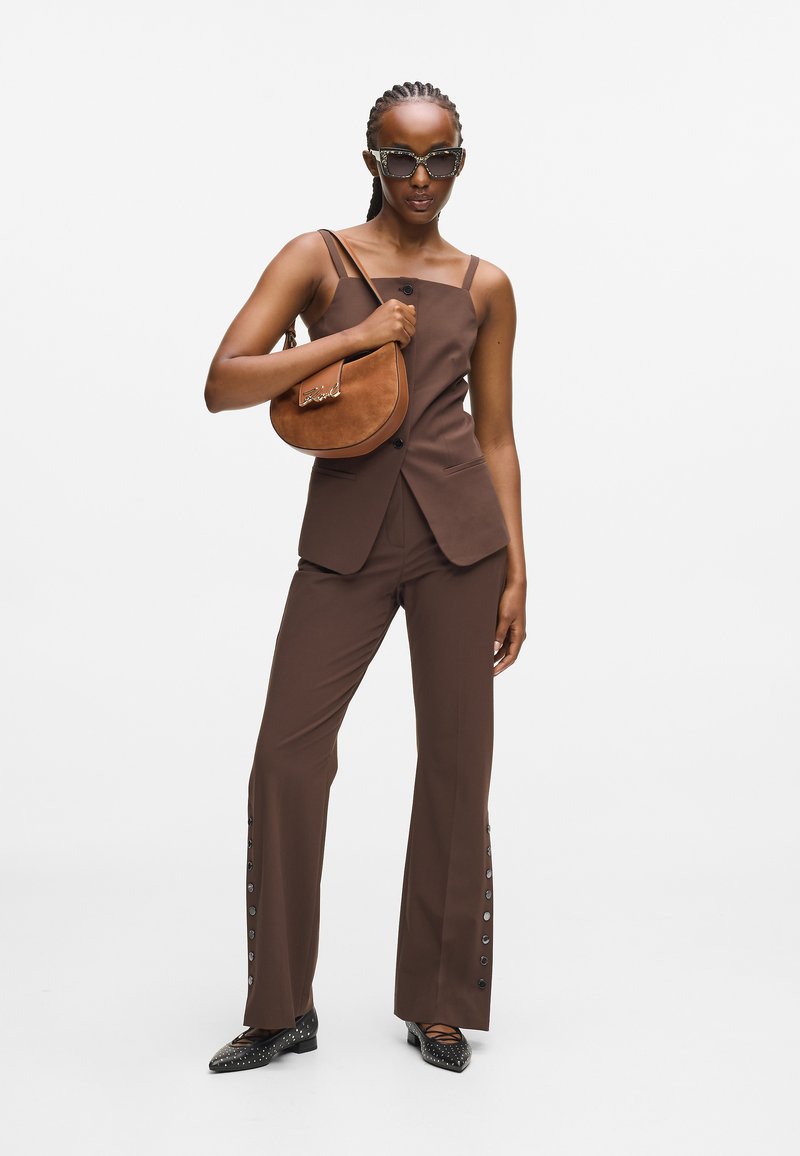 Brun skræddersyet vest og flagrende bukser med knapdetaljer, parret med en brun skuldertaske og sorte nitterede sko. Modellen bærer oversized solbriller.