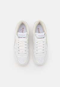Hvite lær sneakers med perforerte detaljer, flate lisser og en beige aksent. Har en logo på tungen og en teksturert såle.