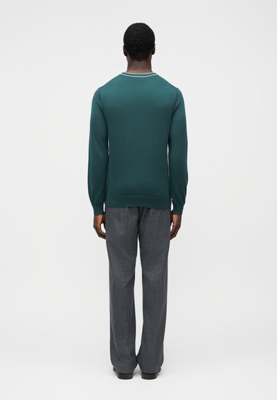 Πλεκτό πουλόβερ τιρκουάζ με στρογγυλή λαιμόκοψη και ριμπ μανσέτες, σε συνδυασμό με γκρι παντελόνια με λεπτές ρίγες. Απλός σχεδιασμός, χωρίς εμφανή μοτίβα ή λογότυπα.