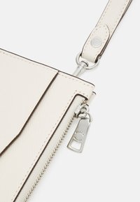 Krämfärgad lädercrossbody-väska med texturerad yta, silverfärgad hårdvara och dragkedjestängning med en märkesdragflik.