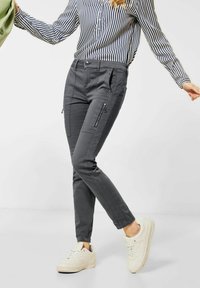 Grå smala byxor gjorda av ett mjukt tyg, med sidofickor med dragkedja, diskret sömnad och en slät yta. I kombination med vita sneakers.