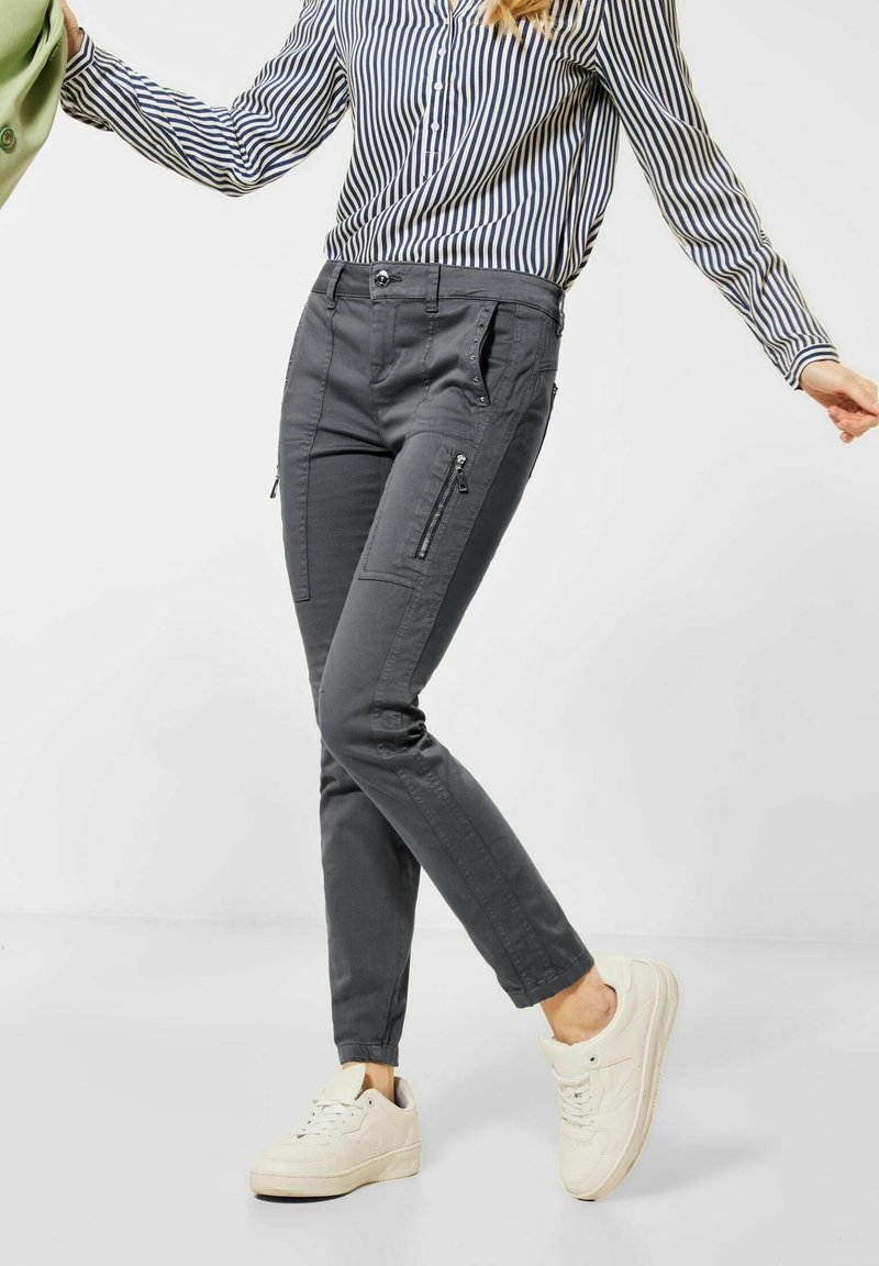 Grå smala byxor gjorda av ett mjukt tyg, med sidofickor med dragkedja, diskret sömnad och en slät yta. I kombination med vita sneakers.