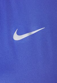 Sportowa tkanina Nike w intensywnym niebieskim kolorze o gładkiej fakturze. Zawiera wyraźnie widoczne srebrne logo Swoosh.