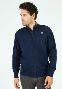 Cardigan zippé marine en tissu tricoté. Doté de poignets et d'ourlet côtelés, de détails de col contrastants et d'un petit emblème sur la poitrine.