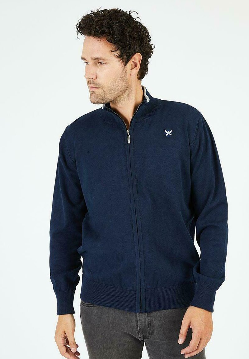 Cardigan zippé marine en tissu tricoté. Doté de poignets et d'ourlet côtelés, de détails de col contrastants et d'un petit emblème sur la poitrine.