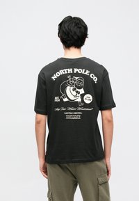 T-shirt de algodão cinza escuro com estampa vintage do Pai Natal nas costas, texto branco e corte descontraído. Mangas curtas e gola redonda.