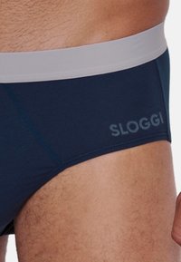 Slip SLOGGI di colore blu navy con una cintura elastica grigio chiaro; tessuto liscio con una vestibilità aderente e dettagli di cucitura sottili.