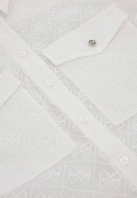 White button-up shirt featuring a textured fabric with embroidered patterns, clear buttons, and a single decorative silver accent at the collar.