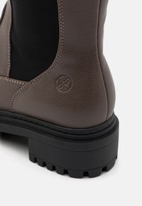 Brune skinn ankelstøvel med svarte elastiske sider, strukturert overflate og robust svart gummisåle. Har preget blomsterlogo detaljer.