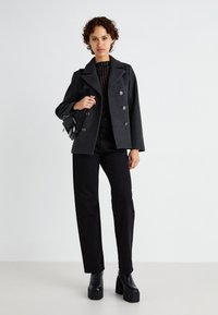 Cappotto peacoat grigio doppiopetto con colletto a scendere, abbinato a pantaloni neri a vita alta e stivali con zeppa. Una borsa a tracolla nera completa il look.