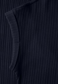 Marineblauer Rippstoff mit einer vertikalen Textur und einer geschwungenen Taschenöffnung auf einer Seite. Das Design ist schlank und an den Körper angepasst.