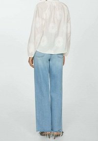 Bílá blůza s květinovou výšivkou a balónovými rukávy; spárovaná se světle modrými širokými džínami. Džínsy mají třepící se okraje a zadní kapsy.