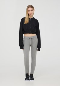 Felpa nera cropped con zip, pantaloni felpati grigi con vita elastica e scarpe da ginnastica nere. Texture lisce e vestibilità rilassata.