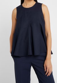 Marinblå ärmlös topp med en utsvängd nederkant, med subtila vertikala sömmar och en slät textur, tillsammans med matchande byxor.