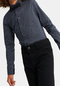 Tmavě šedá košile s dlouhým rukávem a jemným vzorem blesků, klasický límec, přední kapsa, v kombinaci s černými kalhotami a motýlkem.