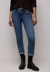 Jeans in denim azzurro chiaro con taglio dritto, orli risvoltati e lievi segni di usura. Abbinati a stivaletti neri. Cuciture semplici e chiusura con bottone.