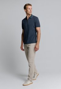 Marineblauwe polo met een ritskraag en witte accenten, gecombineerd met lichtbeige tapered pantalons en witte sneakers met beige details.