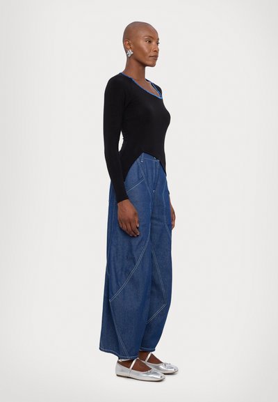 Top a maniche lunghe nera con scollatura azzurra; abbinato a pantaloni in denim a gamba larga con cuciture bianche e vestibilità comoda. Ballerine argento.